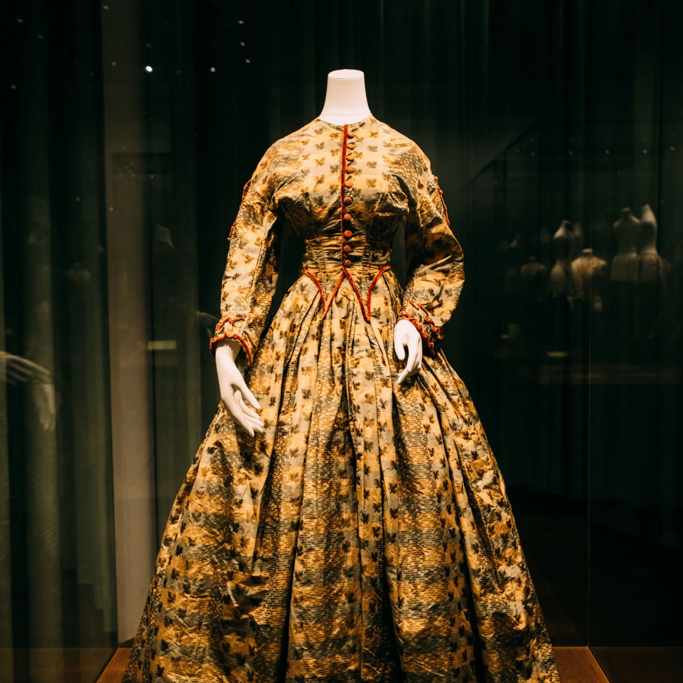 Patterned historic gown on a mannequin in a lit museum display case